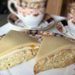 Two cherry flavored Battenberg Scones topped with vanilla buttercream, apricot jam, and marzipan on a Royal Tara plate with two cups of tea in Royal Tara tea cups behind them