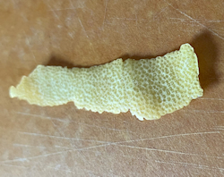 Long yellow lemon peel on brown cutting board.