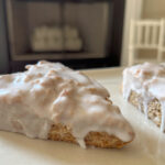 Two pfeffernusse scones with hard opaque anise glaze on a square white plate with an unlit fireplace and children's white rocking chair in the background.